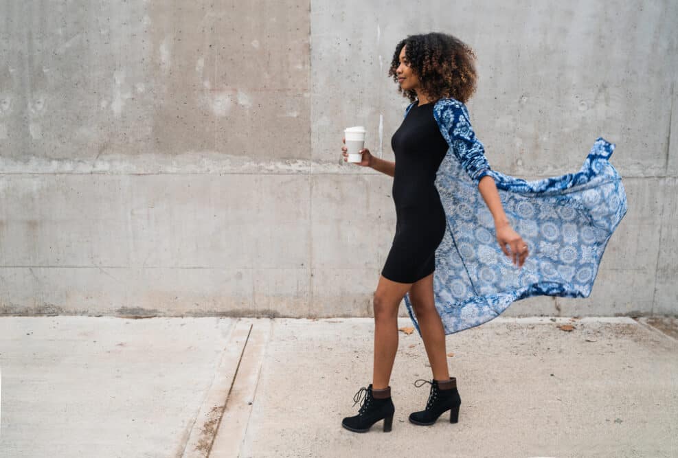 Stylist black lady with a curly hair type walking outside while drinking coffee