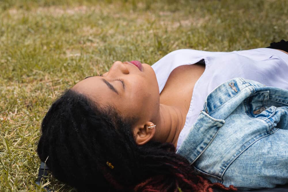 Black lady relaxing outside wearing human hair loc extensions on a 4B hair type