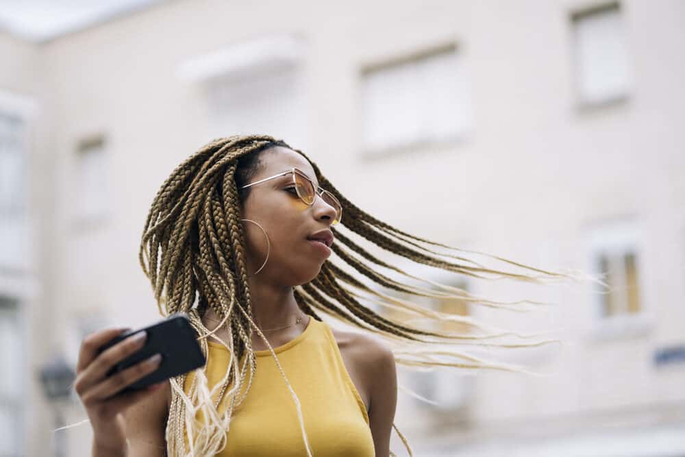 Latin woman with healthy hair under blonde mini braids using an iPhone outside