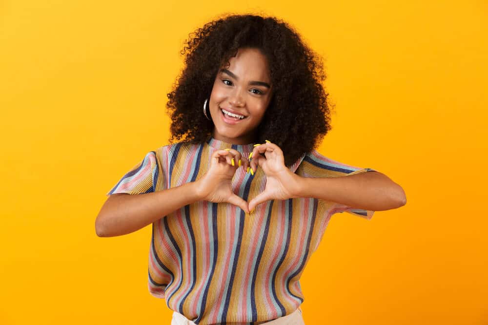 Light-skinned black girl with curly black hair making a sign with her fingers