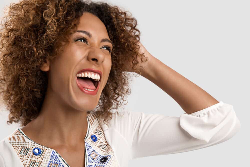 Black lady with curly long locks laughing while rubbing her fingers through her own hair