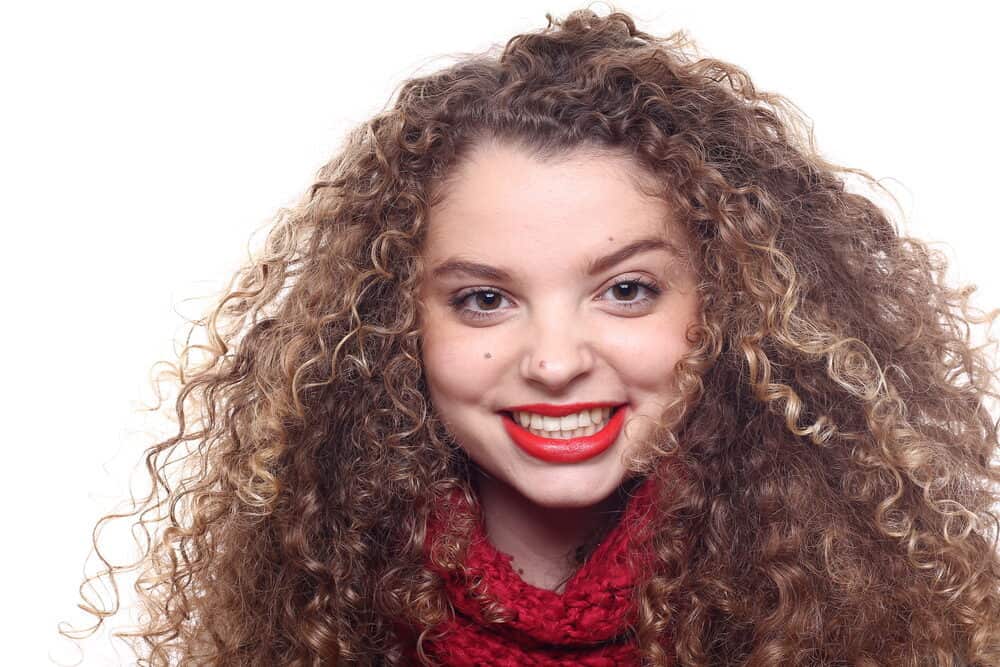 Caucasian lady with a shiny, curly hair texture wearing a red sweater