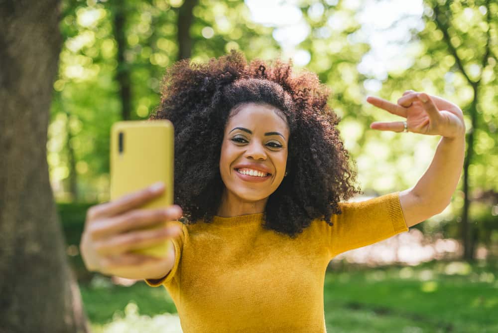 Pretty African girl with curly dry hair taking a selfie outside at the park