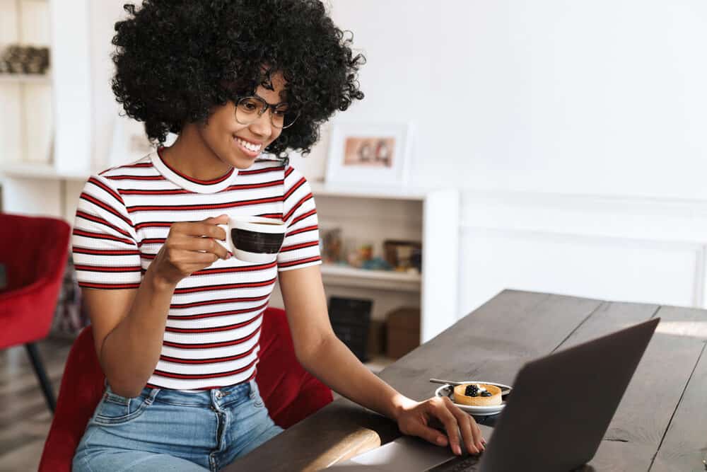 Black girl drinking coffee with bouncy curls created with rollers and a hard hat dryer for home and salon use