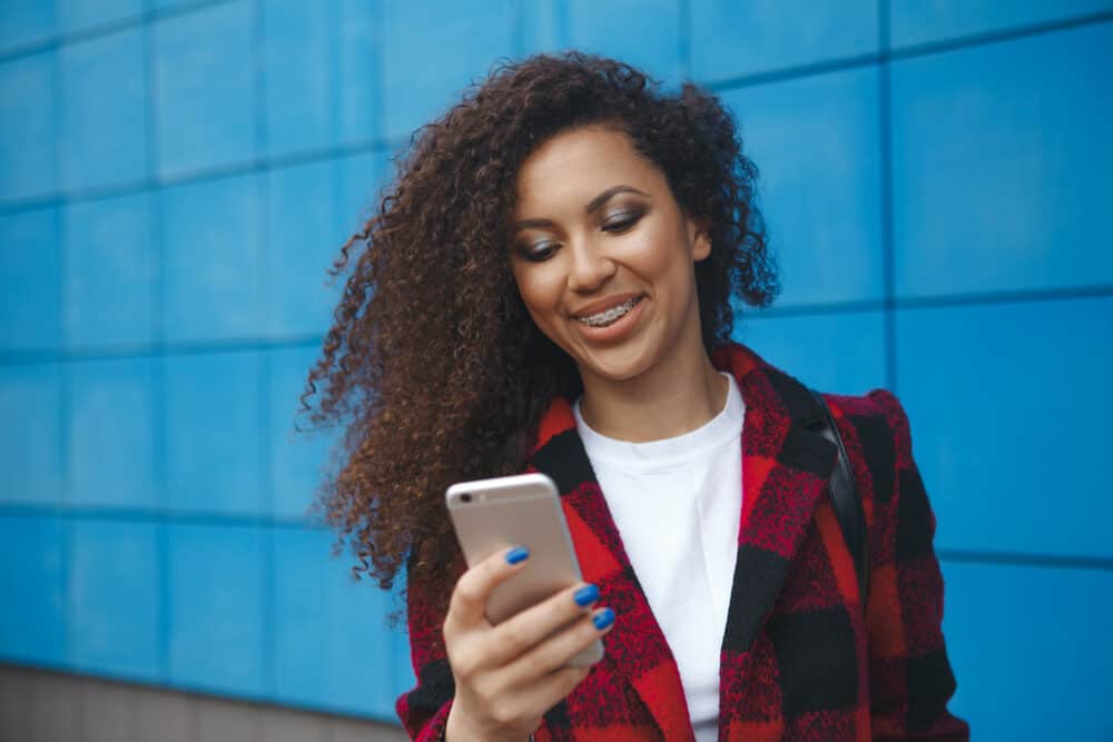 African American female researching thinning hair and damaged hair pores on her iPhone