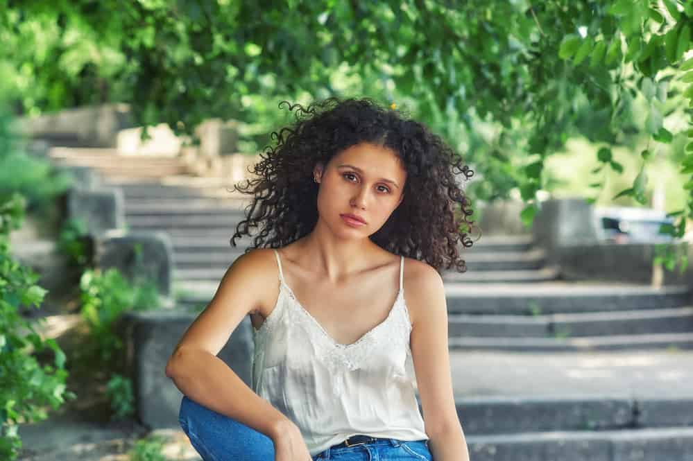Young girl white girl with curly natural hair wearing casual clothes while sitting outside