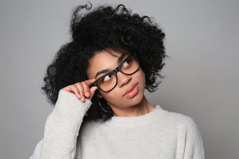 Black lady wearing glasses, pink lipstick, and a gray sweater.