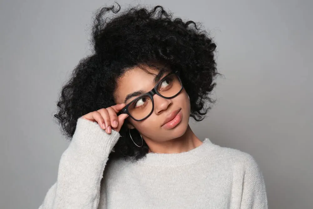 Do Hair Products Expire? Can You Use Expired Hair Products? 9 Black lady wearing glasses, pink lipstick, and a gray sweater.