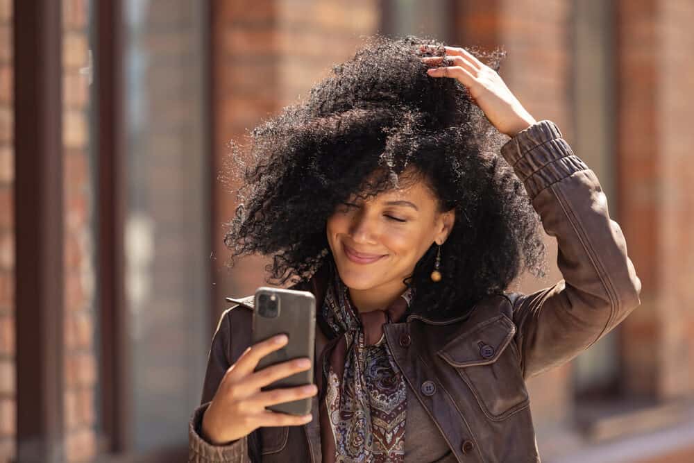 Black woman rubbing her fingers through her curly hair type washed with Herbal Essences shampoo-brand