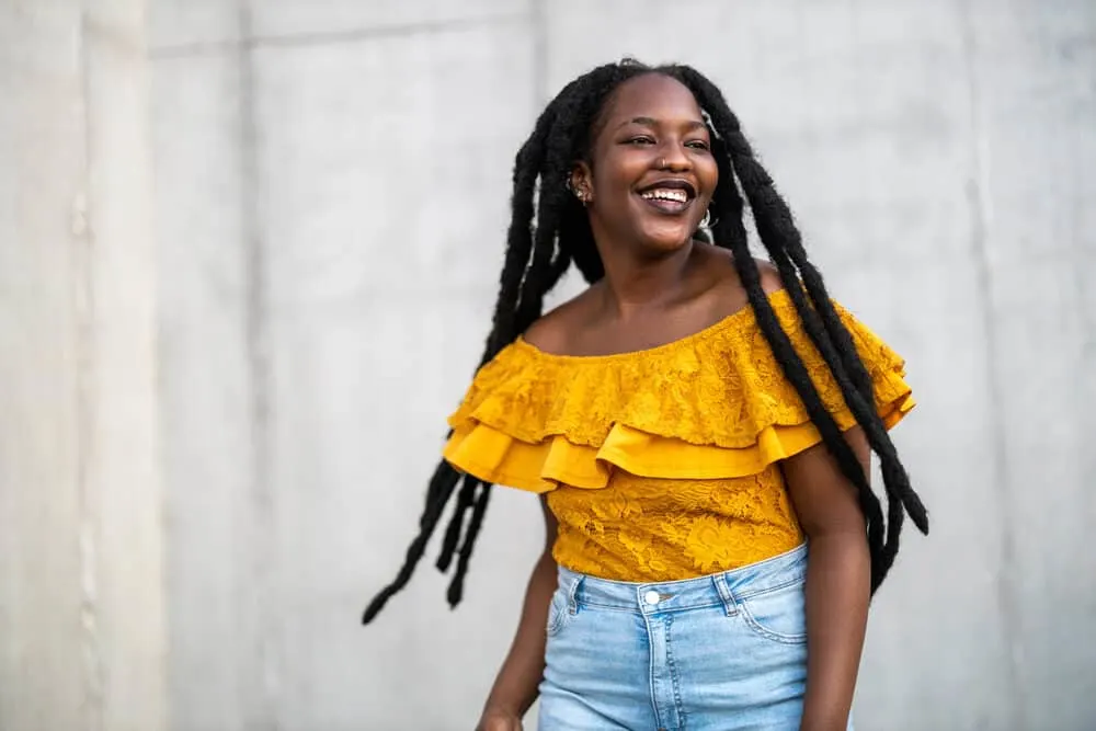 Lady wearing a yellow shirt and blue jeans with wick dreadlocks