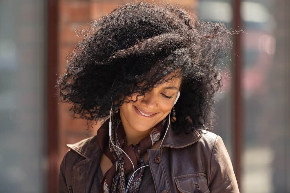 Cute girl listening to headphones with naturally colored hair wearing a dark brown leather coat