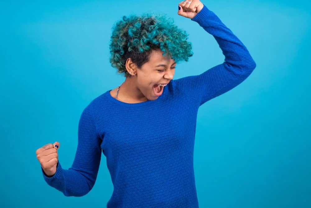 Black girl wearing a midnight blue sweater with electric blue hair dye in textured curly hair