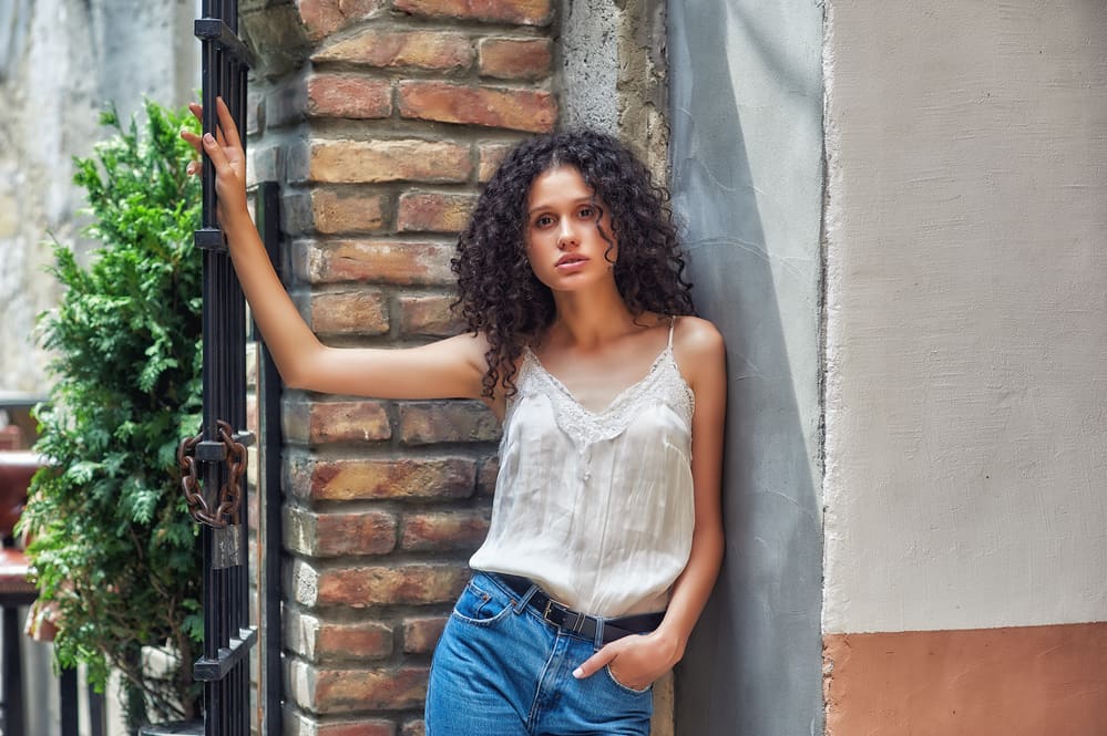 Young lady with brownish-black hair leaving her hair-stylist wearing a white shirt and blue jeans