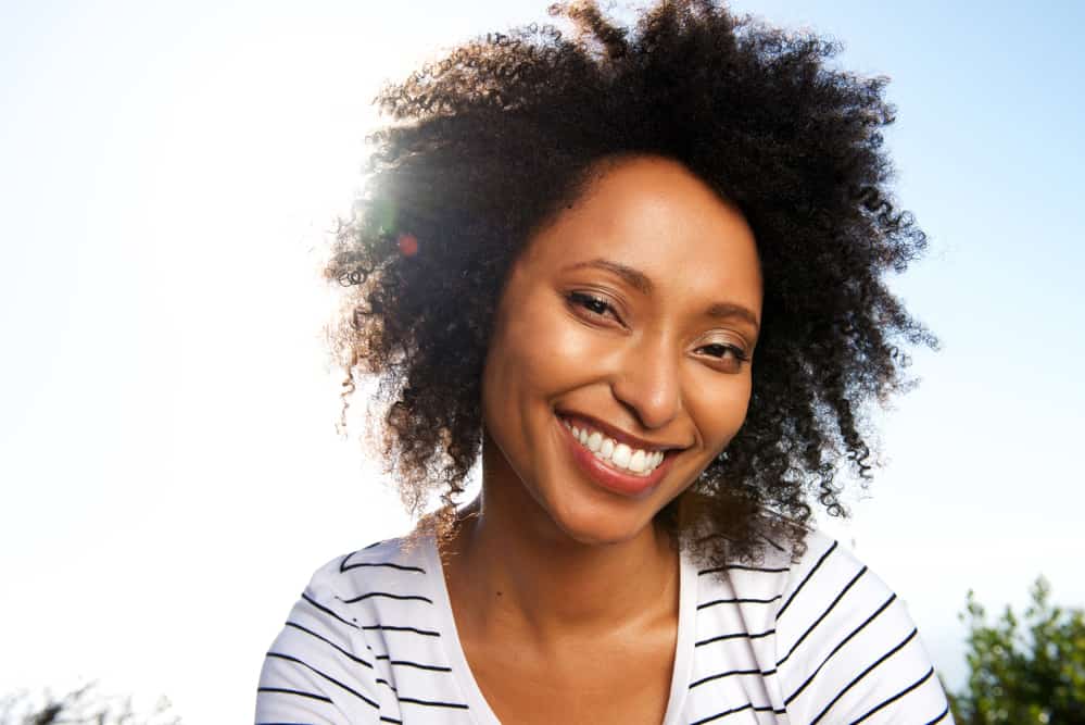 Black lady wearing a striped shirt with curly hair styled with botanical oat milk and argan oil