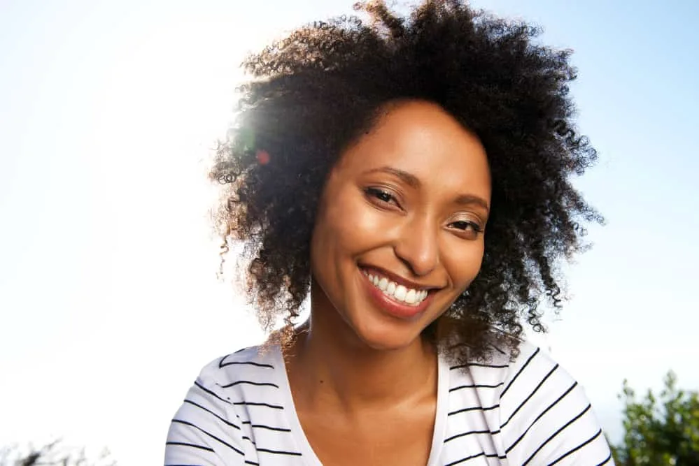 Is Black a Natural Hair Color? Or, Is It Actually Dark Brown? 4 Black lady wearing a striped shirt with curly hair styled with botanical oat milk and argan oil