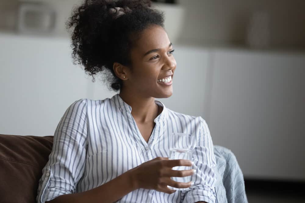 A cute young mixed-race woman with shiny hair drinking a glass of water