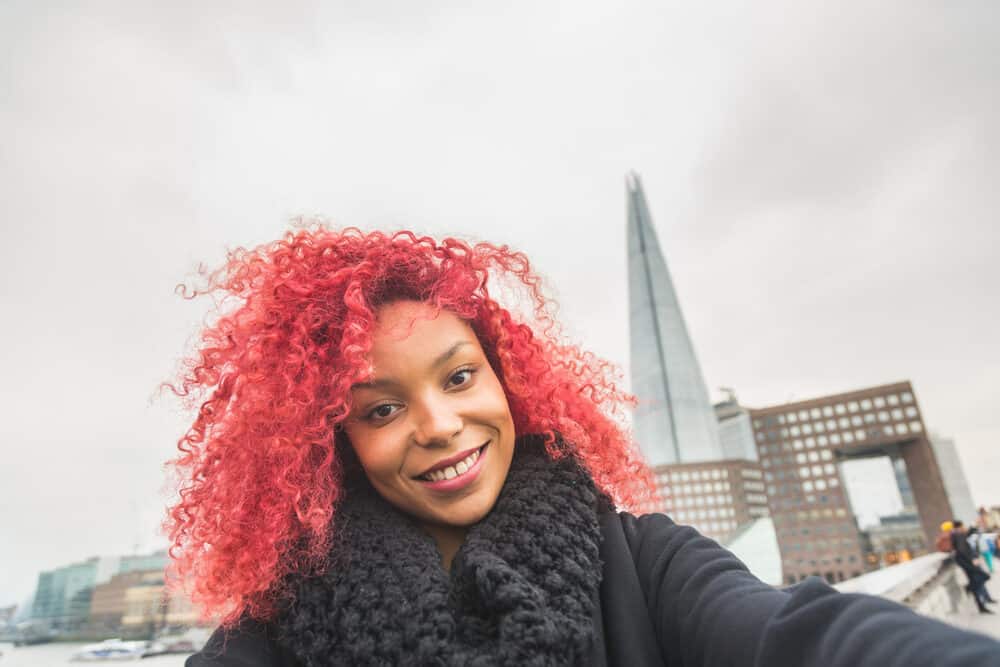 Black girl with red bleached hair in London with skyscraper in the background