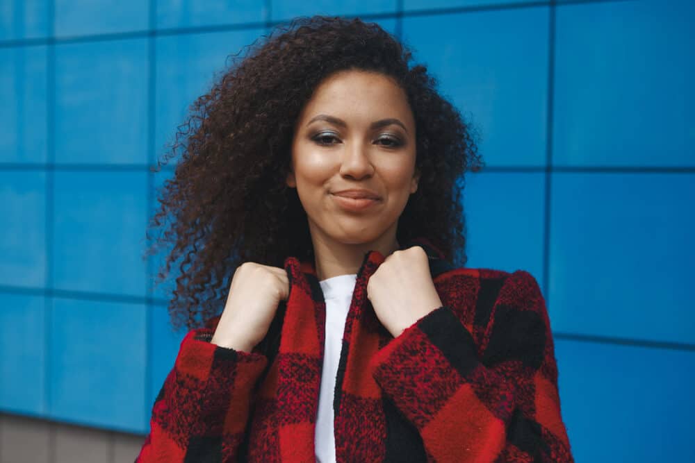 Women with black and red coat and naturally curly hair smiling while looking directly at the camera.