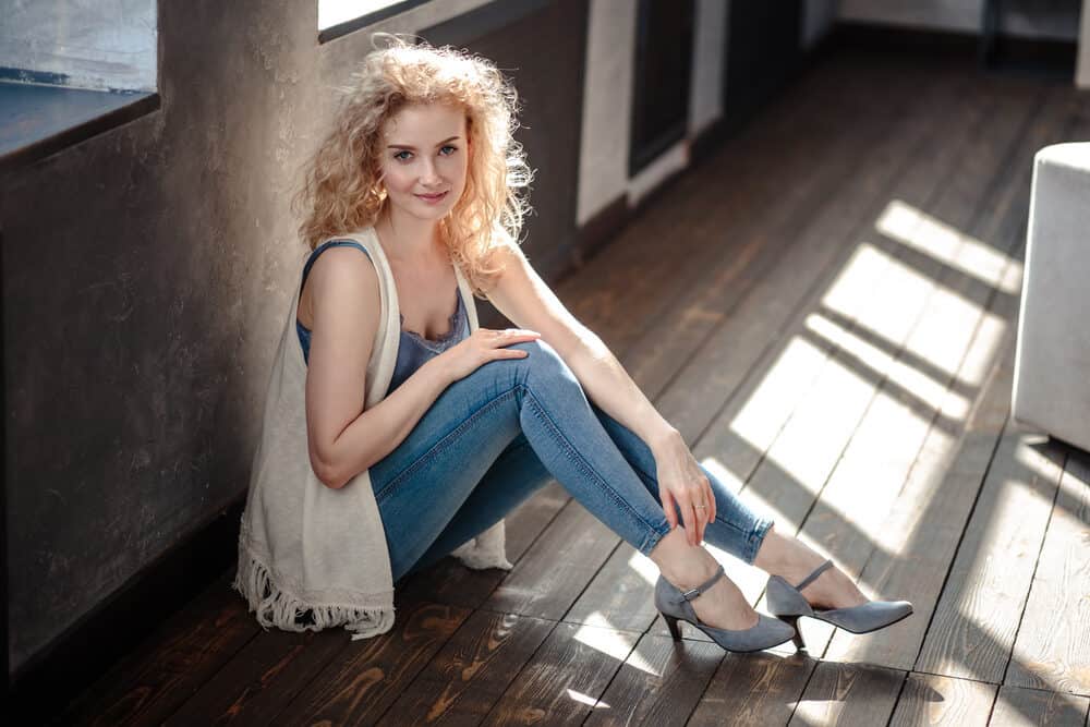 Lady with wavy hair styled with hair oil and water wearing a casual sweater and blue jeans 
