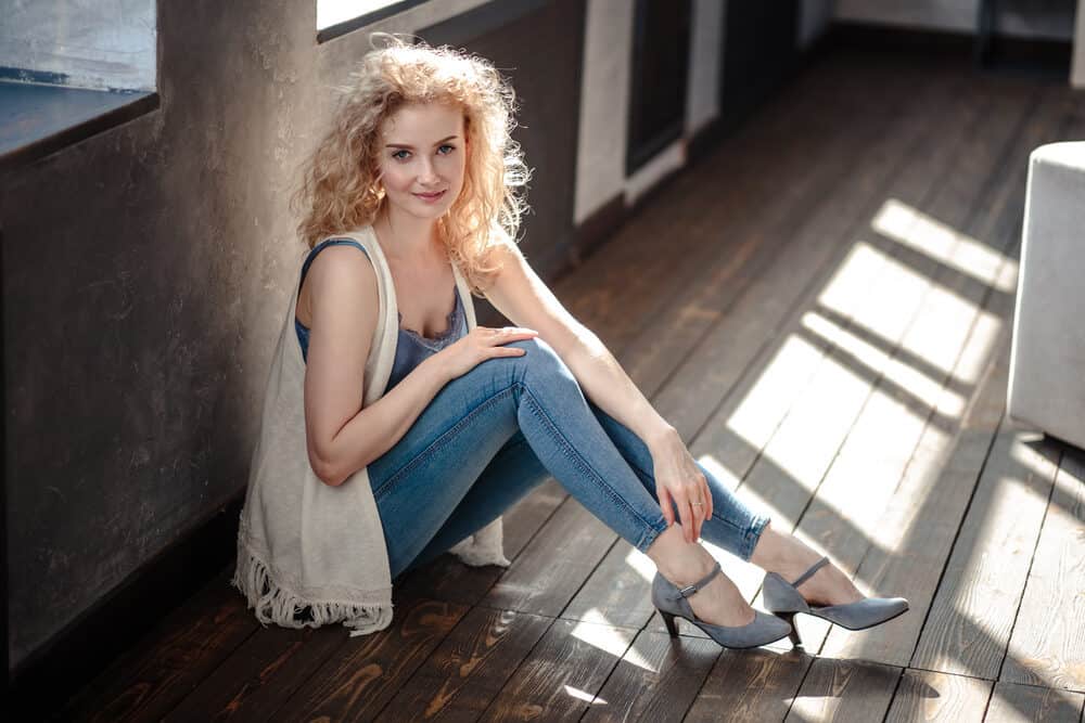 Lady with wavy hair styled with hair oil and water wearing a casual sweater and blue jeans