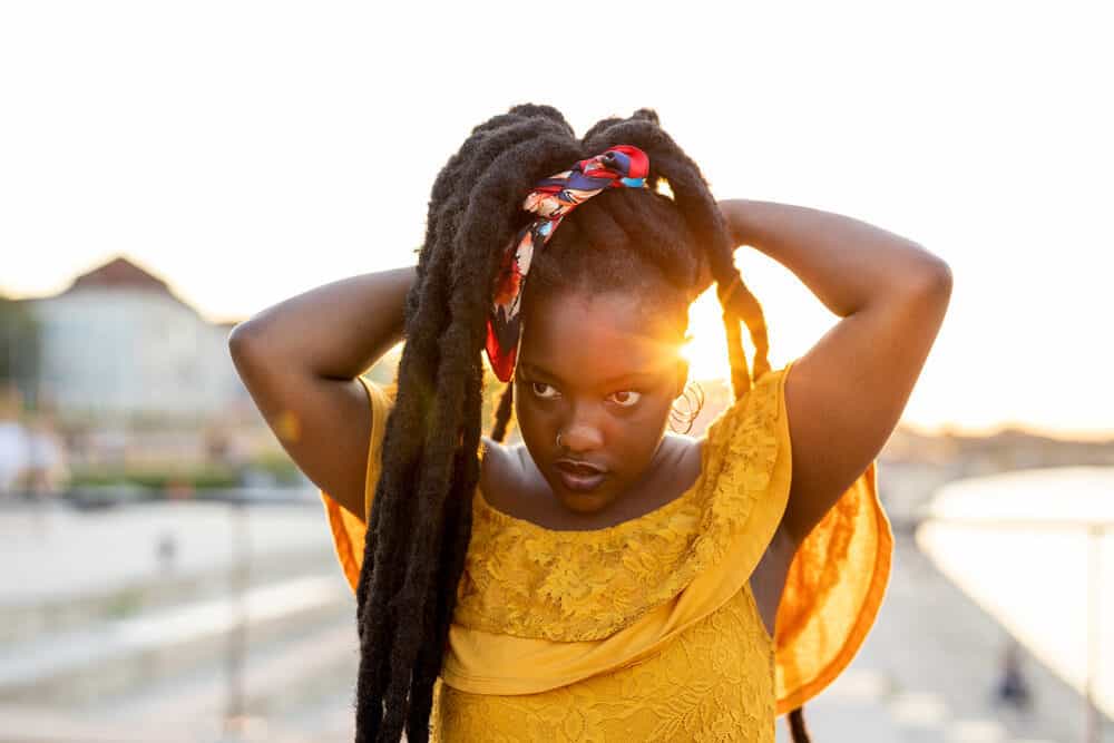 A black girl growing dreadlocks wearing a yellow casual shirt on a warm summer day