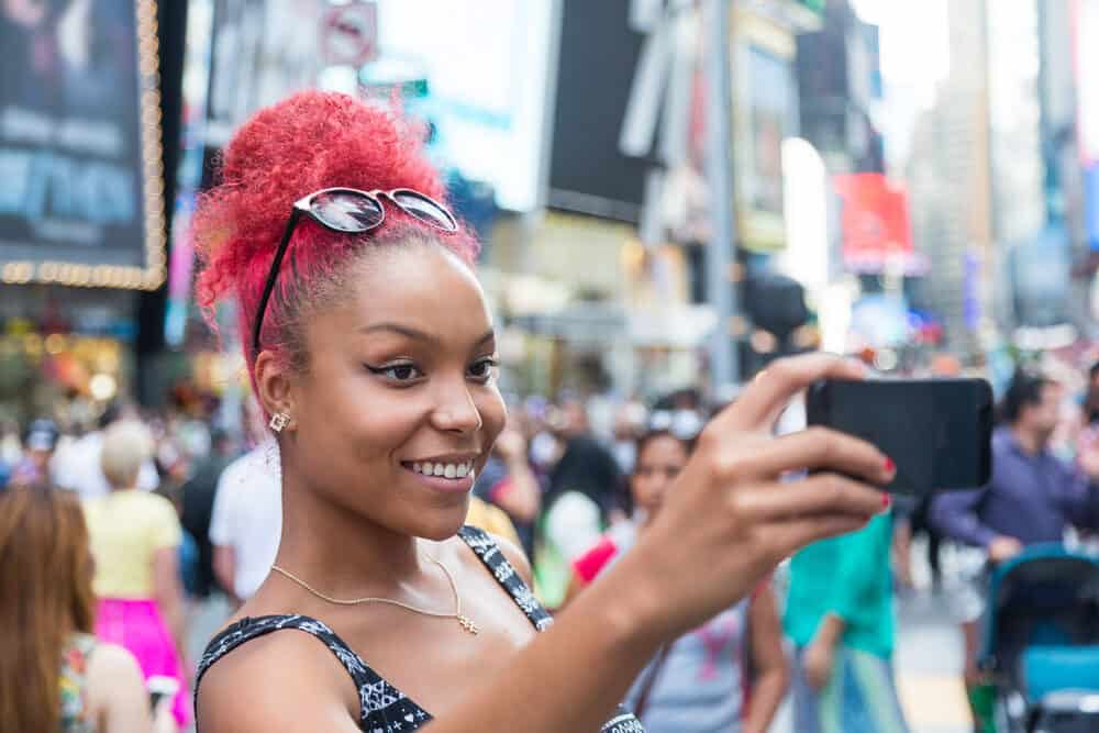 Young woman with red hair and green tones taking a photo with her cell phone outside