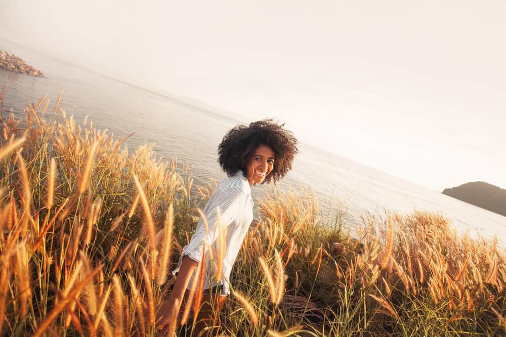 African American female wearing a black and white striped dress shirt and shorts walking beside the ocean