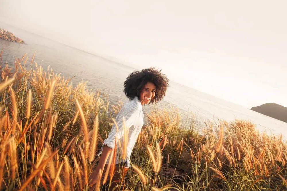 How To Get Vicks Out of Hair With Our Easy Step-by-Step Guide 6 African American female wearing a black and white striped dress shirt and shorts walking beside the ocean
