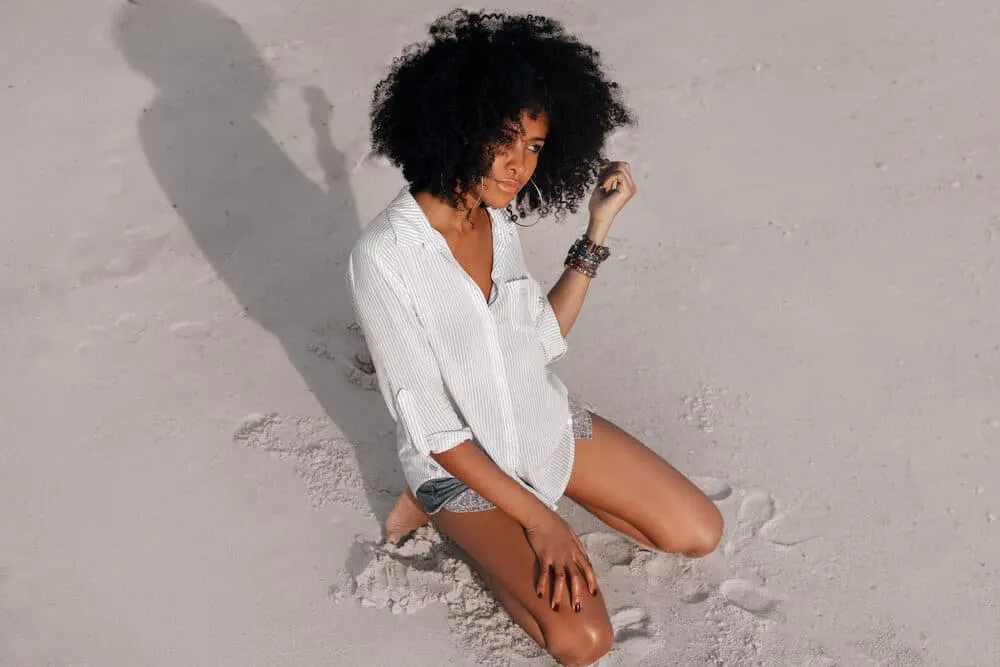 How To Get Vicks Out of Hair With Our Easy Step-by-Step Guide 4 Adult female with type 3C curls playing in the sand at the beach
