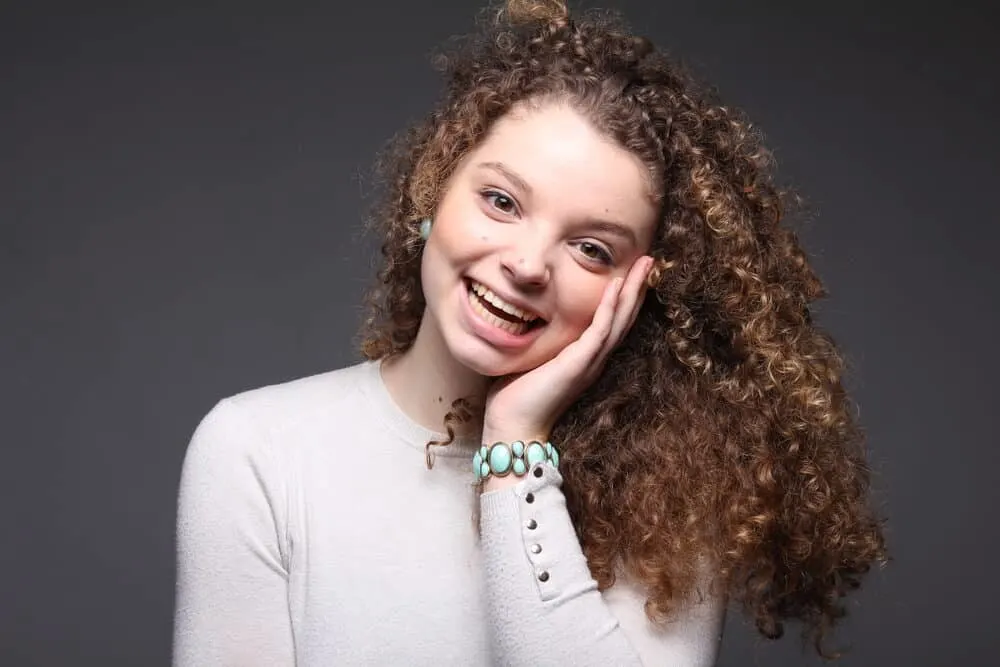 Lady with healthy natural curls wearing an aqua bracelet and light brown sweater 
