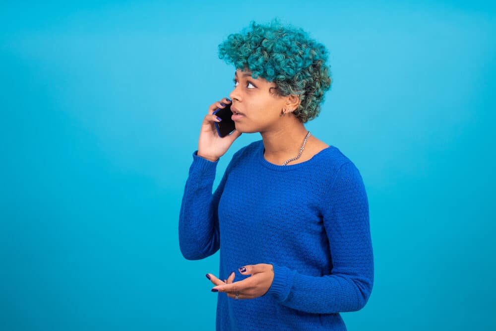 Black lady with a splat midnight hair color wearing curls and a blue sweater