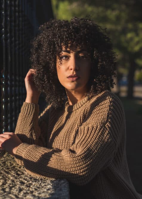 American female with naturally curly hair type, arched eyebrows, and red lipstick leaning on a fence in Yellowstone National Park.