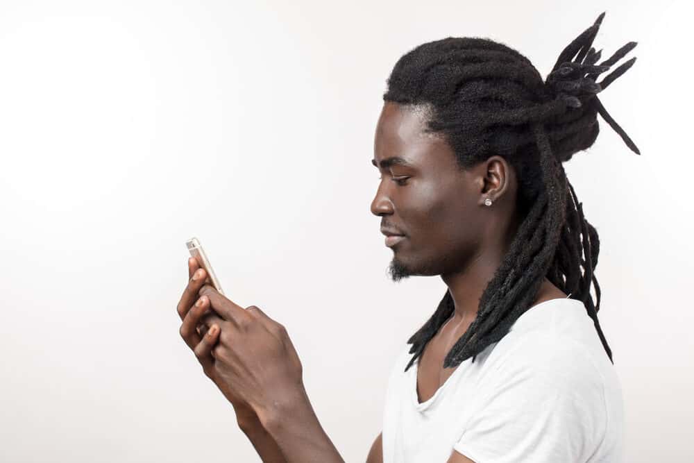 Dude with long hair on a loc journey wearing a white t-shirt while using an iPhone