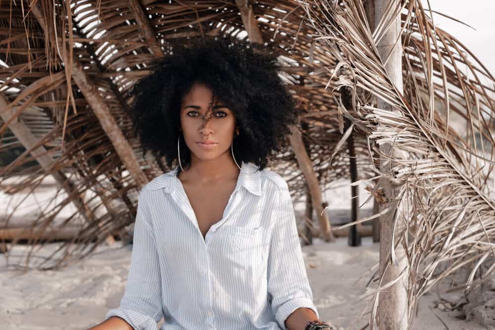 Cute young black mom sitting on a sandy beach with a head full of curls