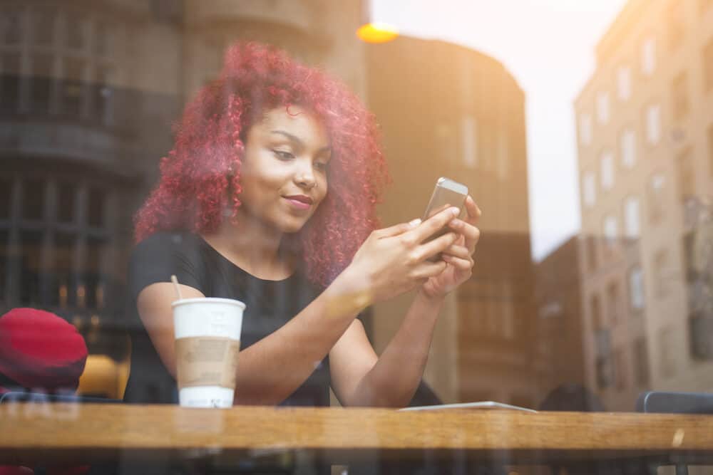 Black lady drinking coffee and using an iPhone with Manic Panic reddish dark hair 