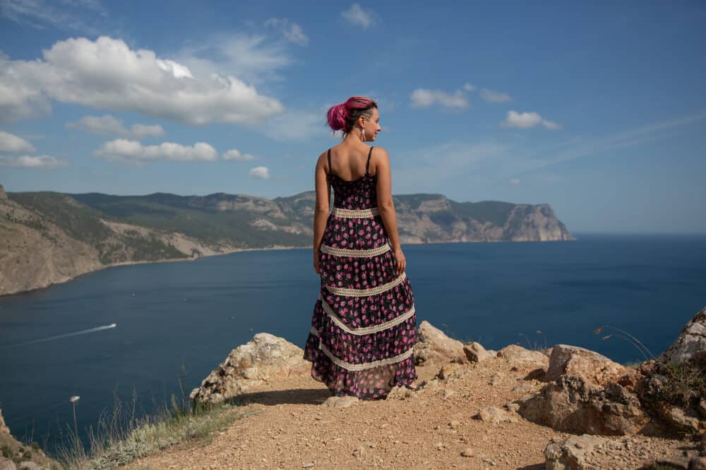 Caucasian female with pink dry hair standing near dirty warm water wearing a colorful dress