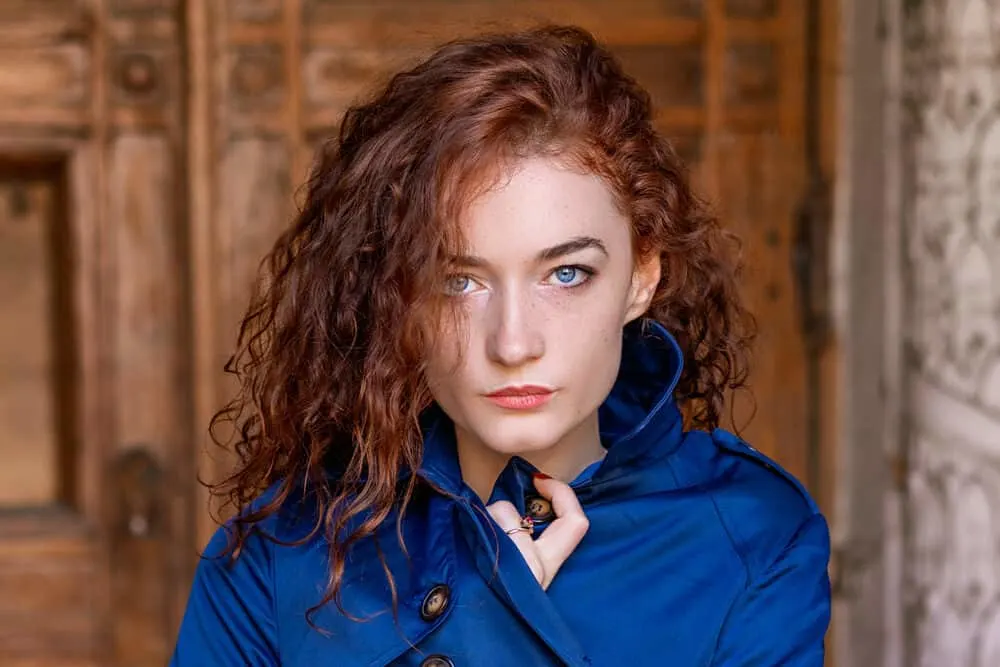 Cute red-haired lady with a wavy hair type wearing a blue jacket and red lipstick