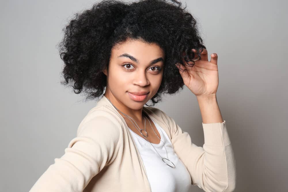 Black female with 4B hair wearing a yellowish-brown sweater and white shirt.