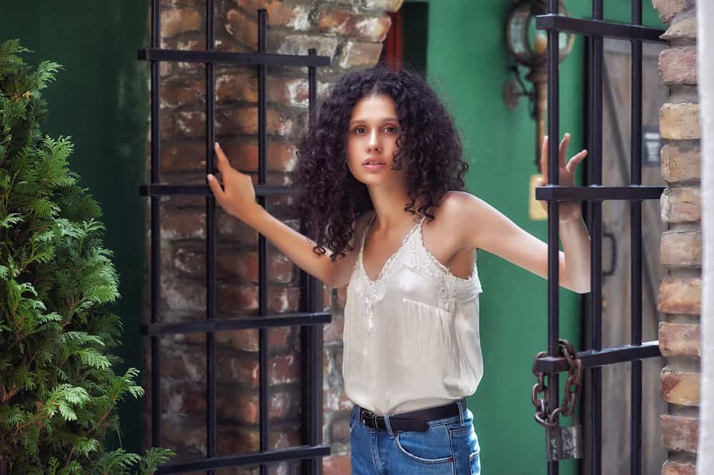 Petty white girl with brown natural hair standing outside between an open gate