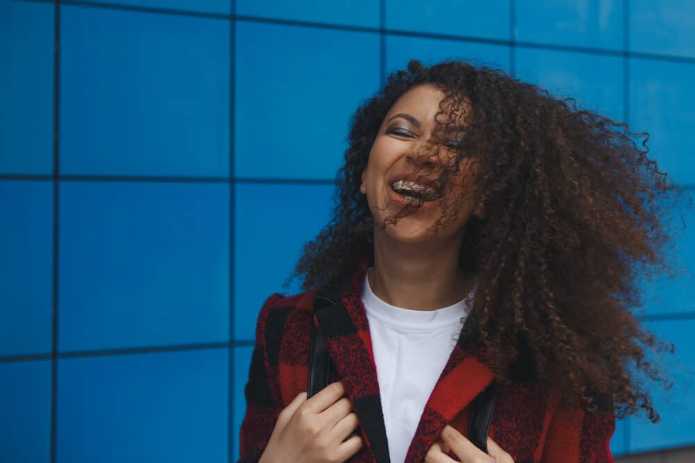 Female with wavy hair strands blowing in her face on a windy day, wearing a huge smile on her face.