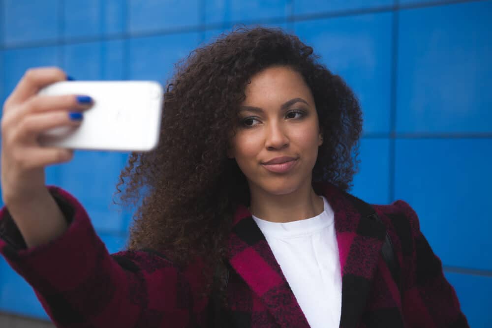 Happy young woman using an iPhone 10s outdoors on a windy spring day.