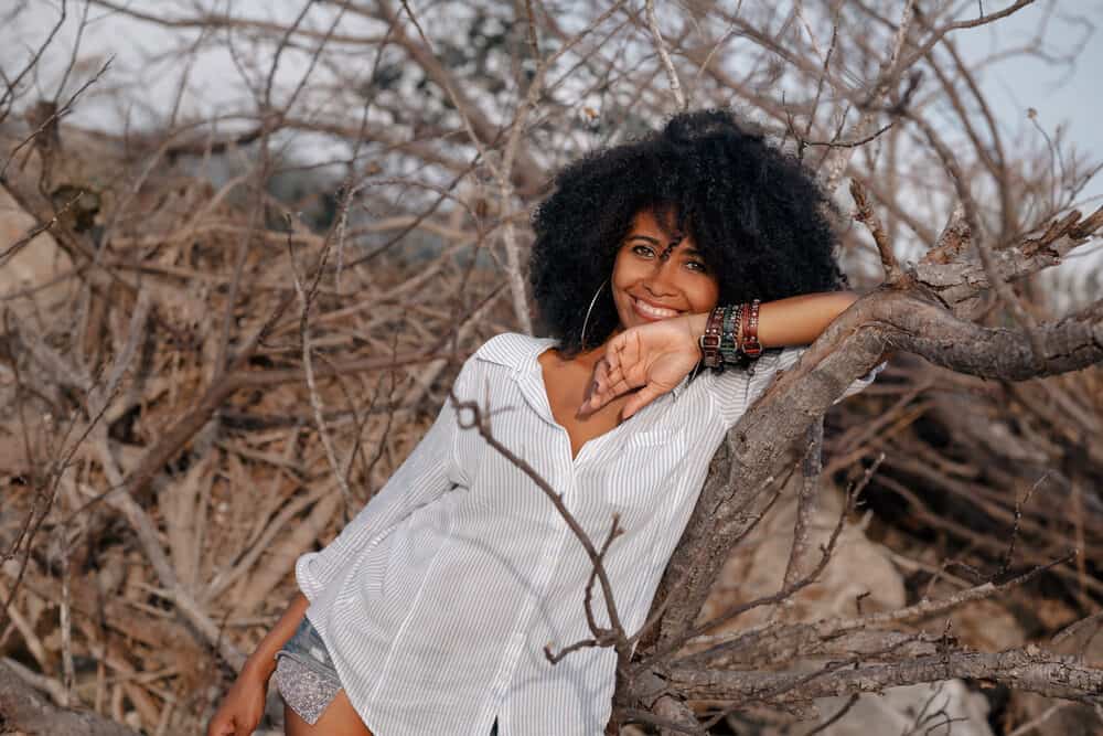 A young black lady standing in the woods with bouncy curls styled with several aromatic essential oils