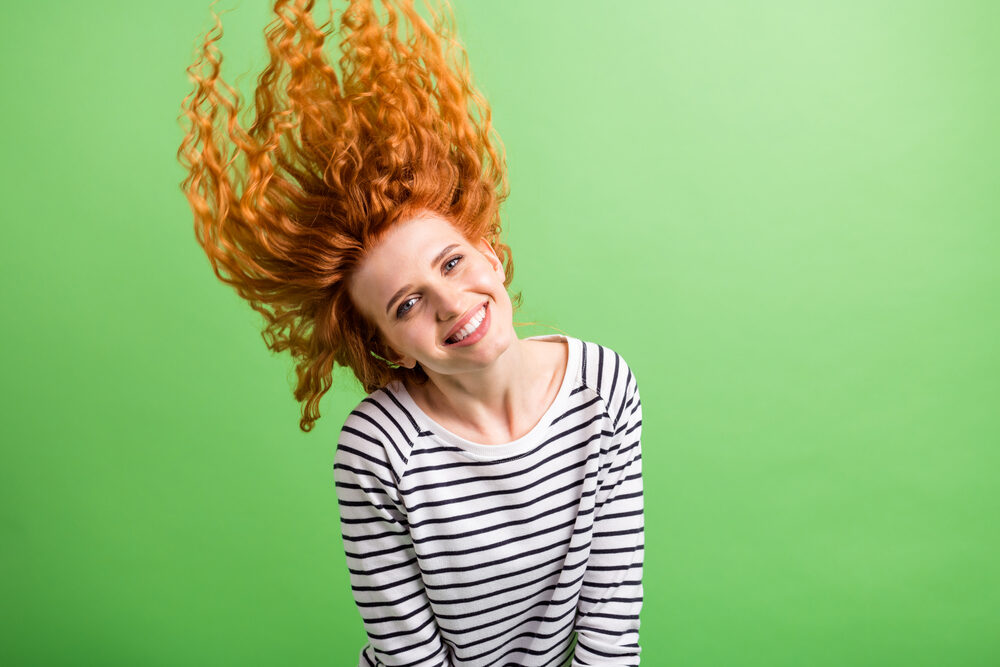 Pretty lady with curls that are a reddish natural color wearing a striped shirt with raven black strips. 