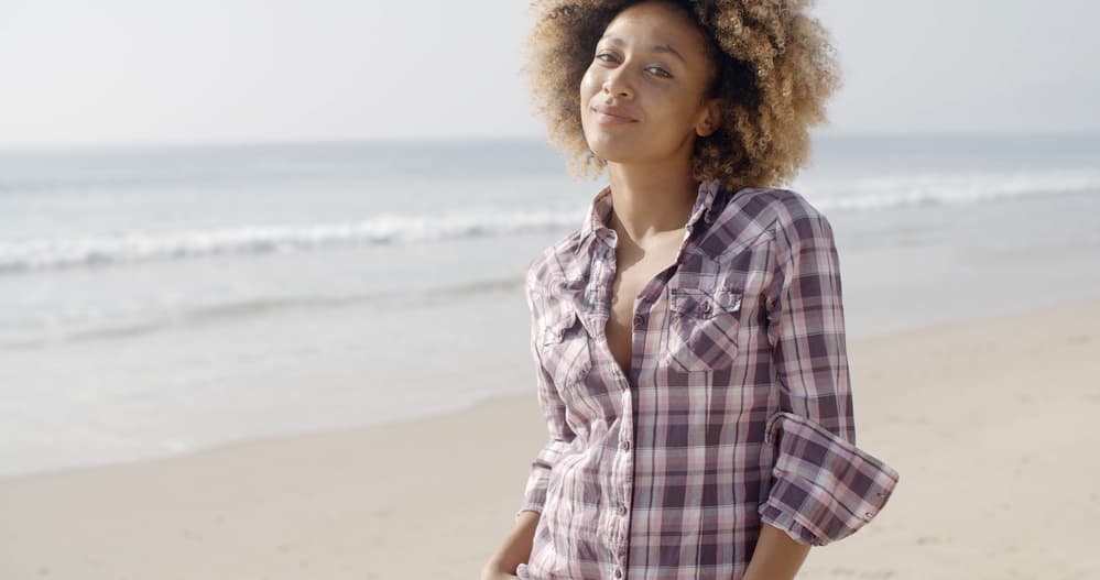 Beautiful African American lady with wet hair while walking through the sand at the beach.