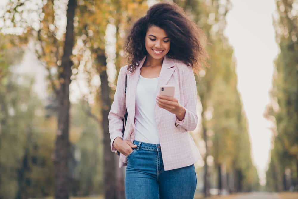 African American female with normal hair walking through the park reading about dangerous ingredients.