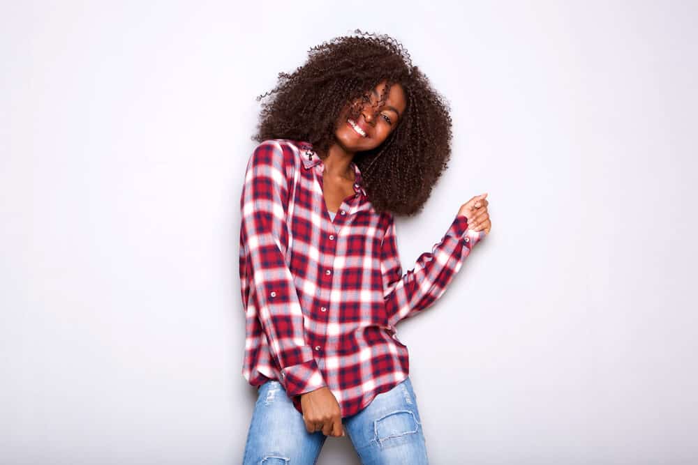 Stylish young African woman in checkered shirt preparing to braid hair before bedtime.