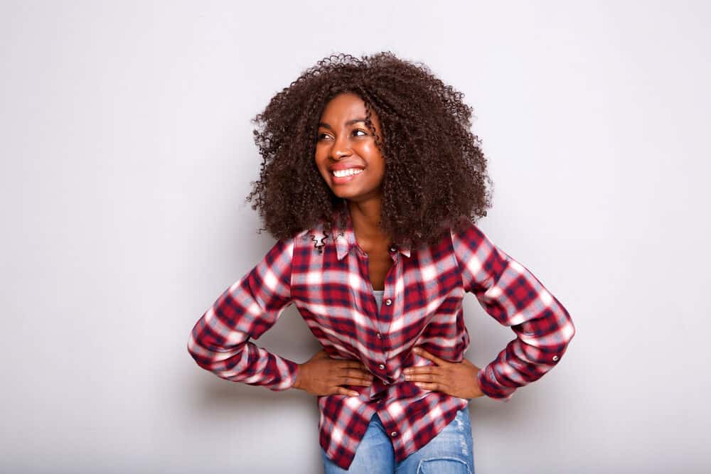 Black girl with curly natural hair styling wearing a plaid shirt with her hands on her hips.