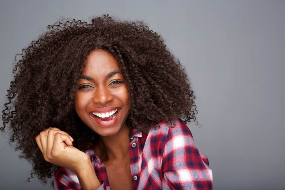 Cheerful African American lady with curly natural hair and extensions from a professional hair stylist.
