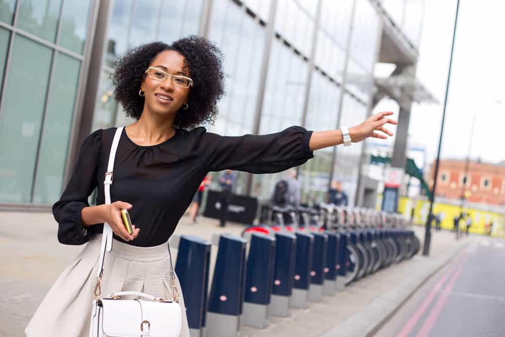 Lady with curly hair follicles wearing casual clothing calling a taxi.