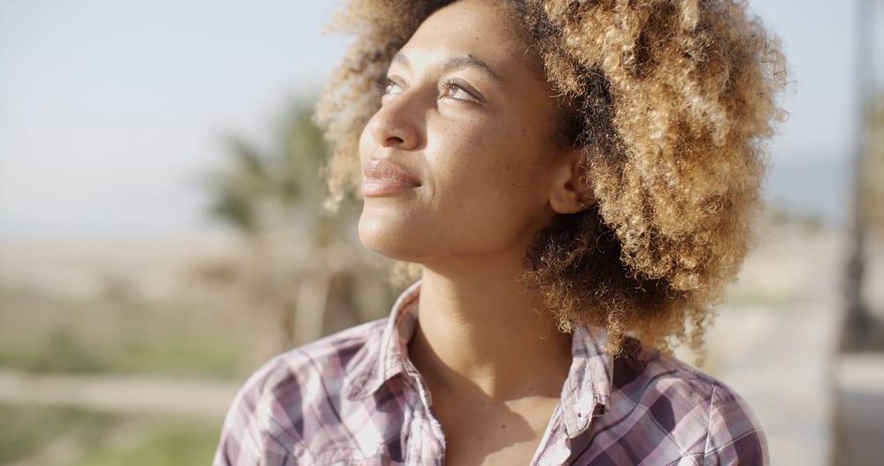 How to Bleach Bath Hair at Home To Remove Color Safely 6 Young African woman on a sunny day with her 4C hair dyed blonde with medium brown undertones.